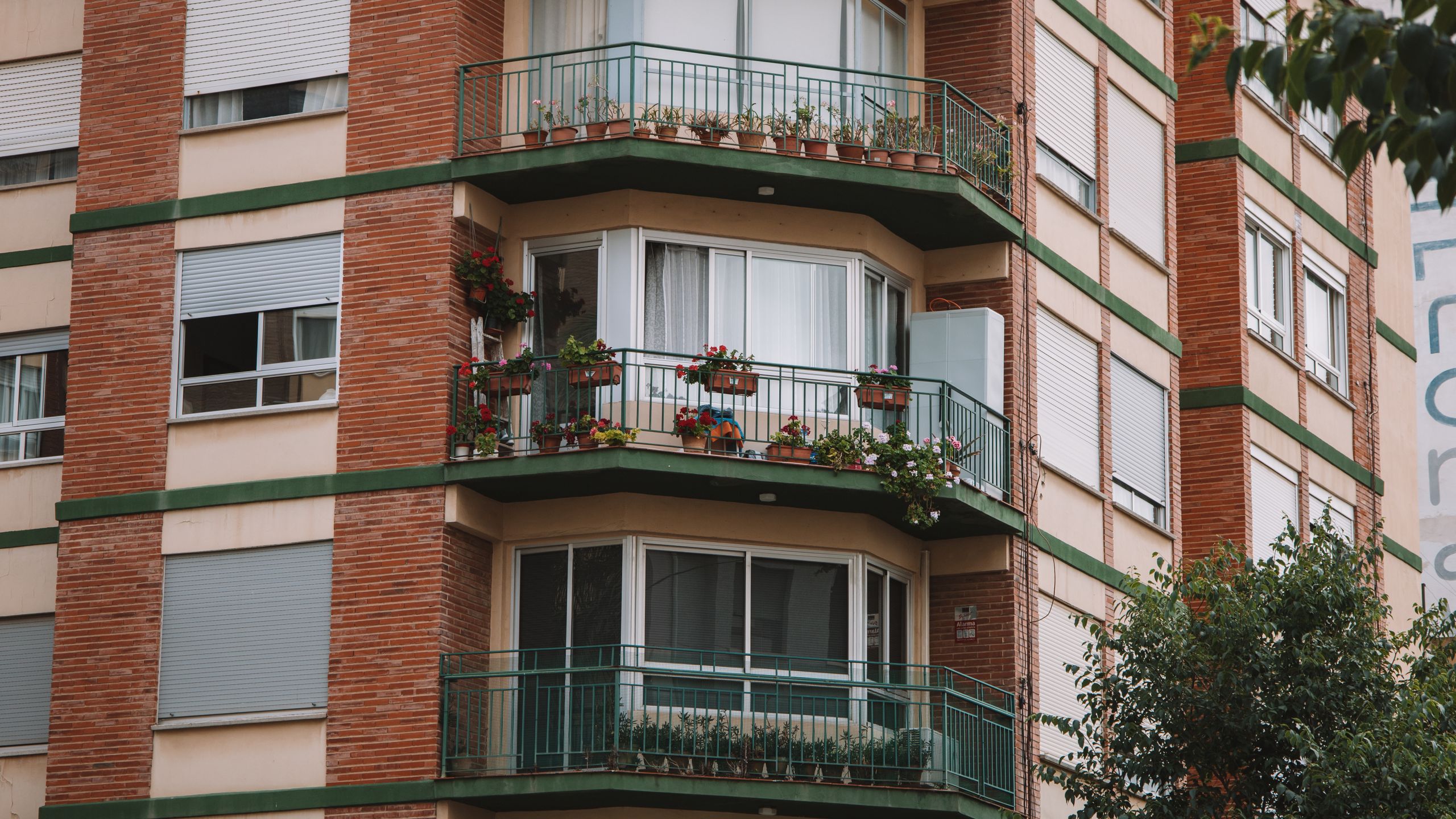 Fachada de un edificio de viviendas de ladrillo con balcones y macetas en Valencia