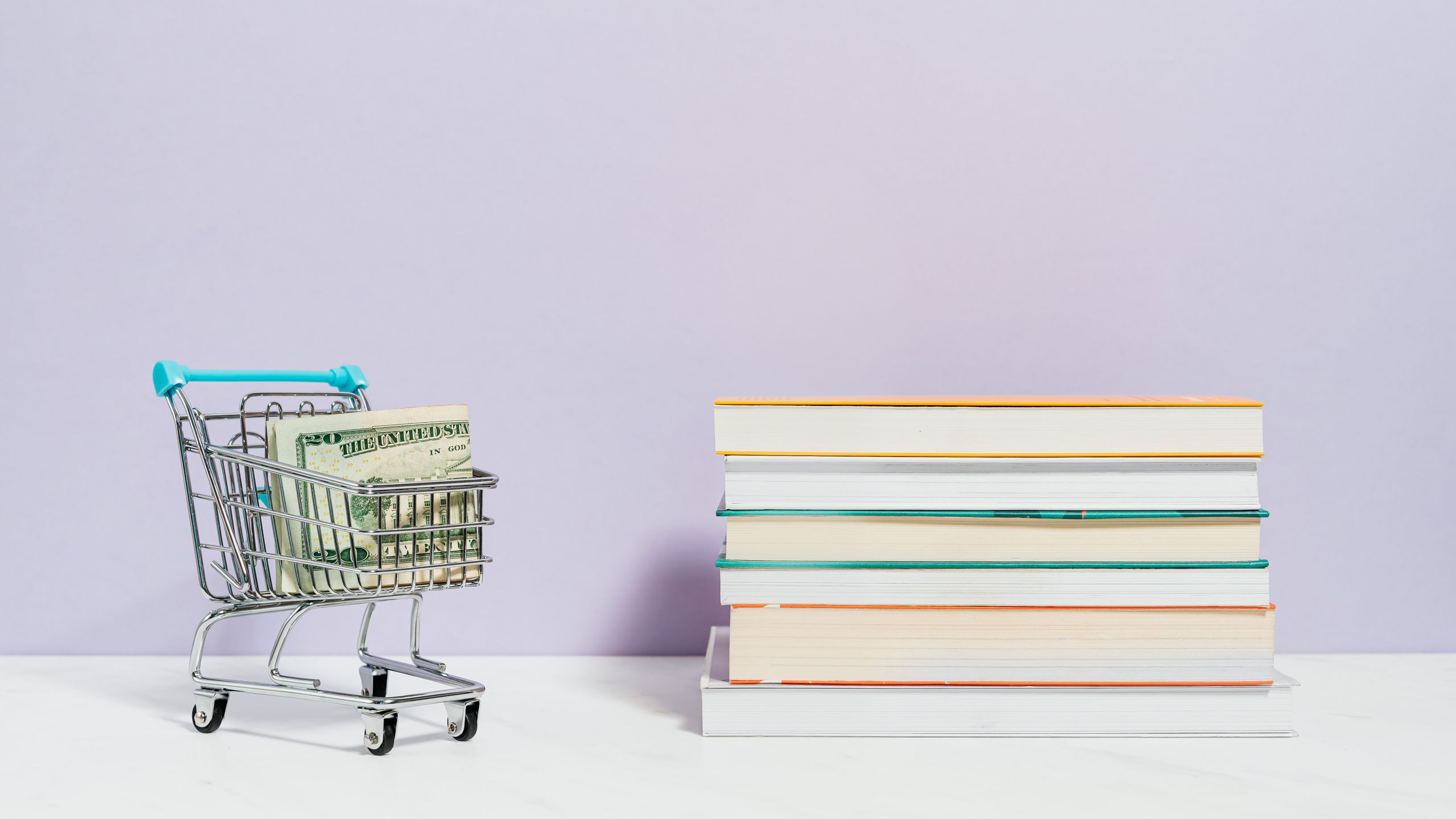 Carrito de la compra en miniatura con billetes junto a una pila de libros de texto, símbolo de los gastos de los hijos que cubre la pensión de alimentos